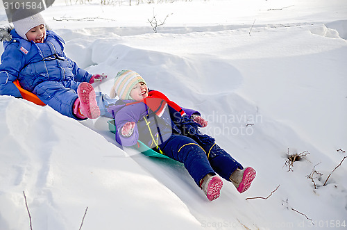 Image of Two girls rolling down a hill in snow