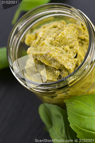 Image of Glass jar with basil pesto on a black plate