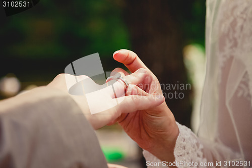 Image of mans hand putting a wedding ring on the brides finger