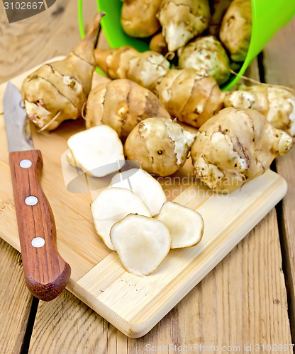 Image of Jerusalem artichokes cut with knife and green bucket on board