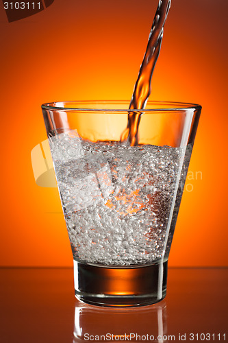 Image of pour water into a glass on orange background