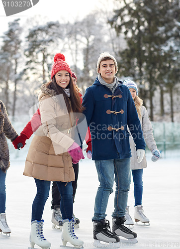 Image of happy friends ice skating on rink outdoors