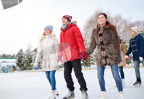 Image of happy friends ice skating on rink outdoors