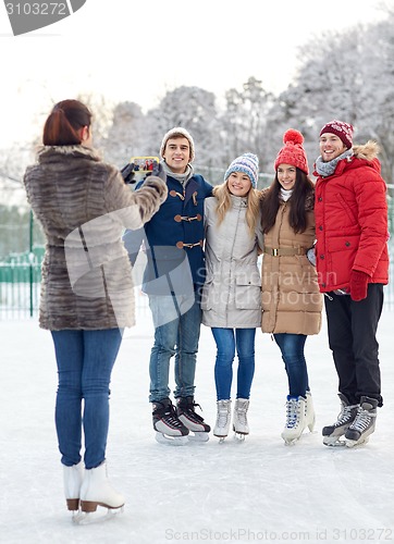 Image of happy friends with smartphone on ice skating rink