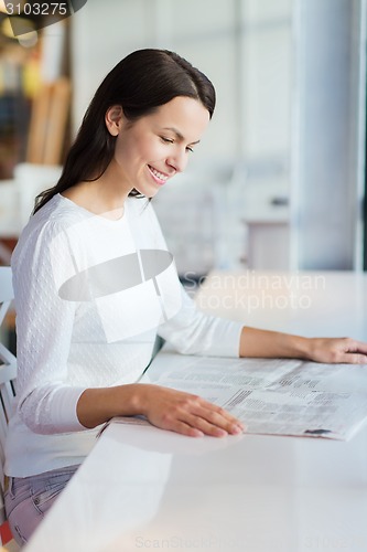 Image of smiling young woman reading newspaper at cafe