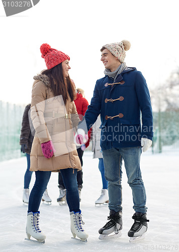 Image of happy friends ice skating on rink outdoors