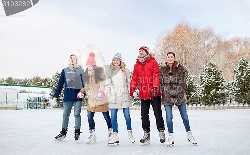 Image of happy friends ice skating on rink outdoors