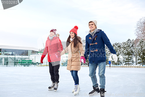 Image of happy friends ice skating on rink outdoors