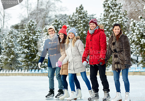 Image of happy friends ice skating on rink outdoors