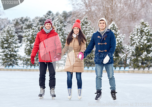 Image of happy friends ice skating on rink outdoors