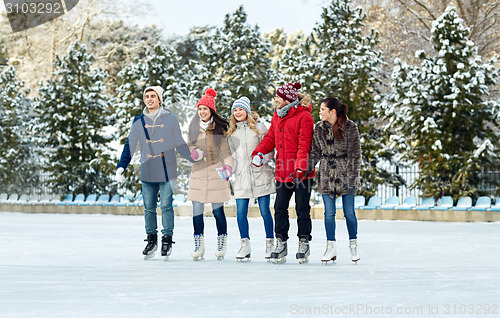 Image of happy friends ice skating on rink outdoors