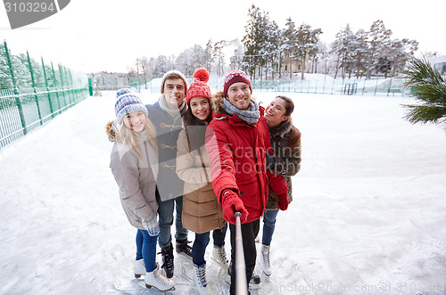 Image of happy friends with smartphone on ice skating rink