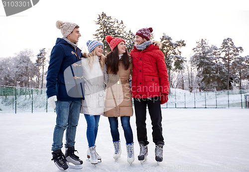 Image of happy friends ice skating on rink outdoors