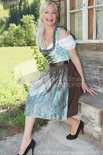 Image of Smiling woman in dirndl sitting on an old bench