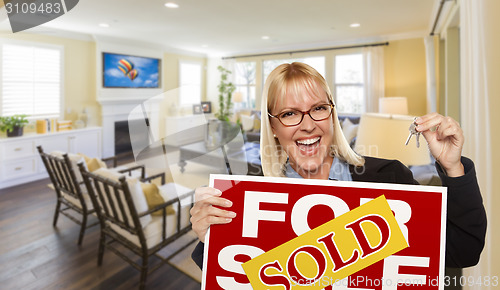 Image of Young Woman Holding Sold Sign and Keys Inside Living Room