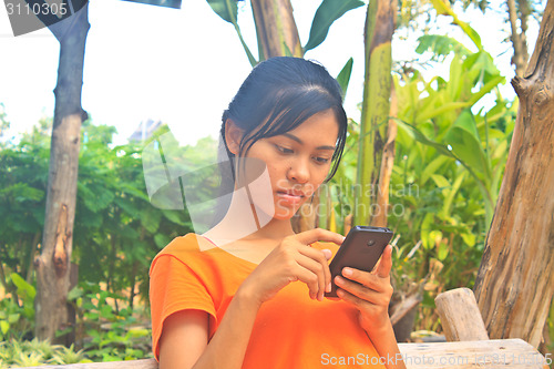 Image of Young girl sitting on the wooden swing with mobile phone