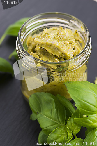 Image of Glass jar with basil pesto on a black plate