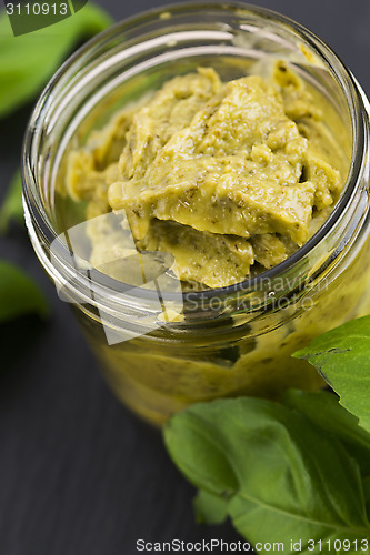Image of Glass jar with basil pesto on a black plate