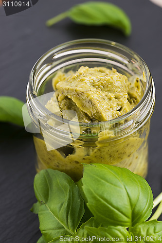 Image of Glass jar with basil pesto on a black plate