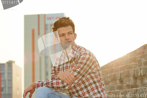 Image of Handsome man outdoors sitting on stone stairs