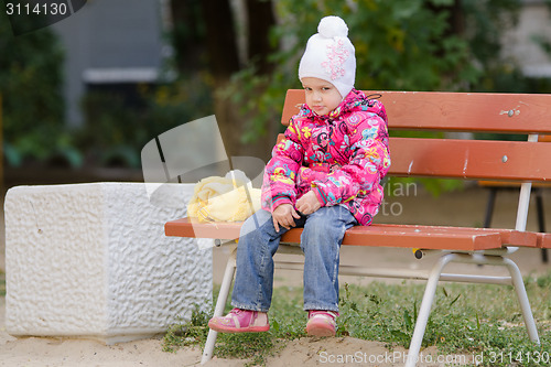 Image of Gloomy girl in autumn clothes sitting on a bench