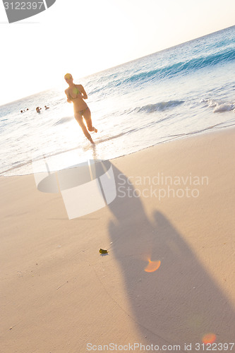 Image of Woman running on the beach in sunset.