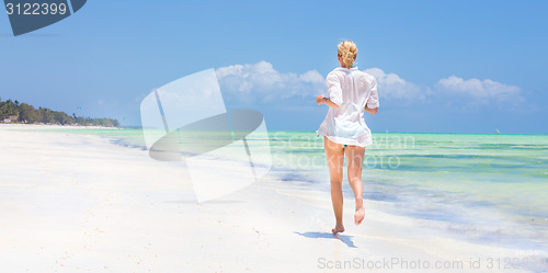 Image of Woman running on the beach in white shirt. 