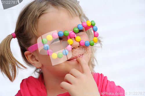 Image of Portrait of cute little girl wearing funny glasses, decorated with colorful sweets, smarties, candies