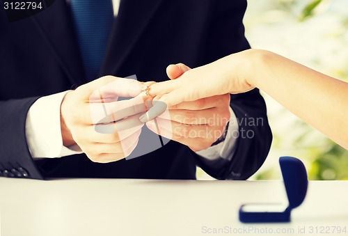 Image of man putting  wedding ring on woman hand