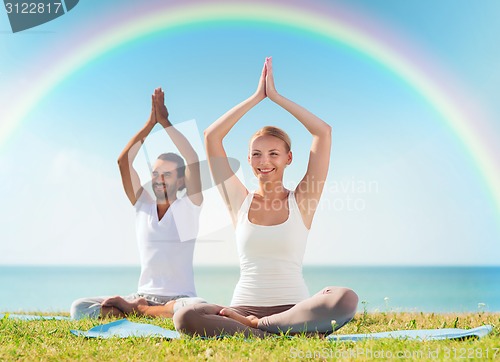 Image of smiling couple making yoga exercises outdoors