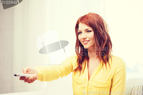 Image of smiling young woman with tv remote control at home