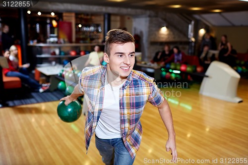 Image of happy young man throwing ball in bowling club