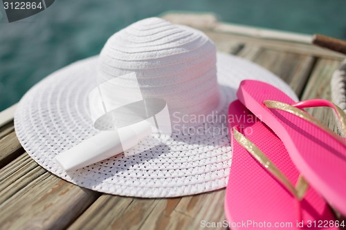 Image of close up of hat, sunscreen and slippers at seaside