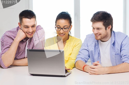 Image of three smiling colleagues with laptop in office