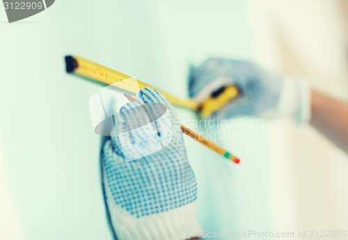 Image of closeup of male in gloves measuring wall with tape