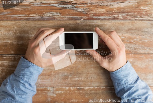 Image of close up of male hands with smartphone on table