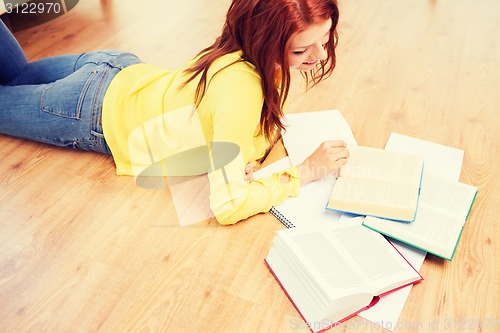 Image of smiling teenage girl reading books on floor