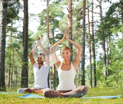 Image of smiling couple making yoga exercises outdoors