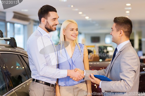 Image of happy couple with car dealer in auto show or salon