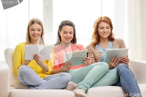 Image of three smiling teenage girls with tablet pc at home