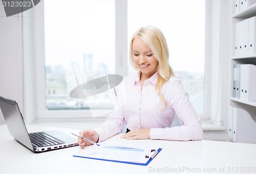 Image of smiling businesswoman reading papers in office