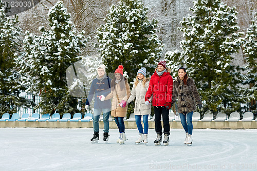 Image of happy friends ice skating on rink outdoors