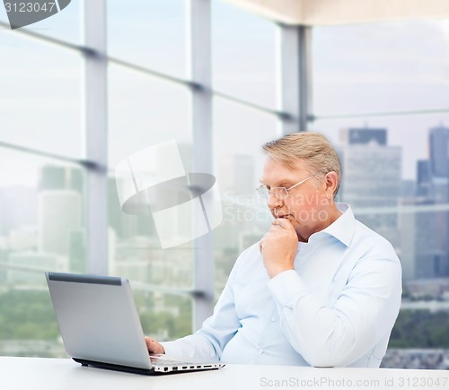 Image of senior man in eyeglasses with laptop at office