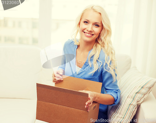 Image of smiling young woman opening cardboard box at home