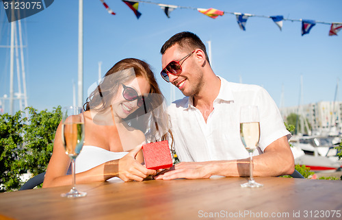 Image of smiling couple with champagne and gift at cafe
