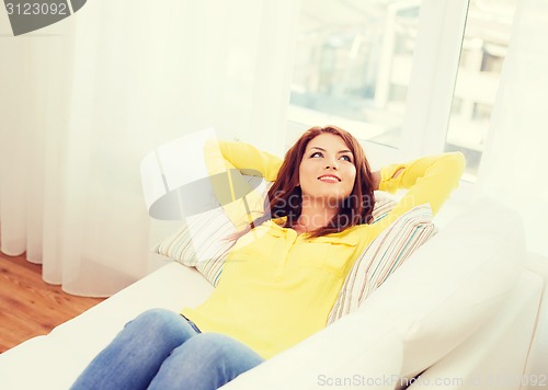 Image of smiling young woman lying on sofa at home