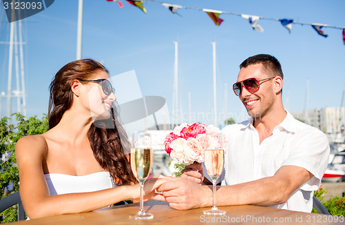 Image of smiling couple with bunch and champagne at cafe