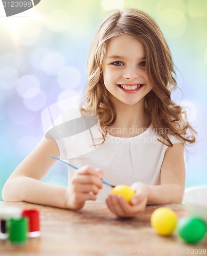 Image of happy girl with brush coloring easter eggs