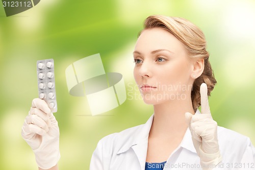 Image of young female doctor with pills pointing finger up