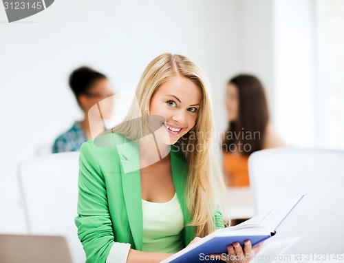 Image of smiling student girl reading book at school